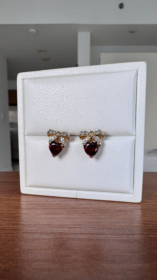 Heart-shaped garnet earrings with diamond bow tops in a white jewelry box.