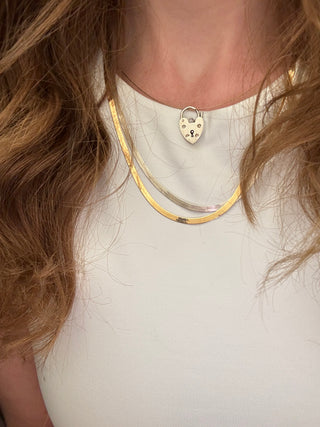 Heart padlock charm styled among layered necklaces worn at the neckline.