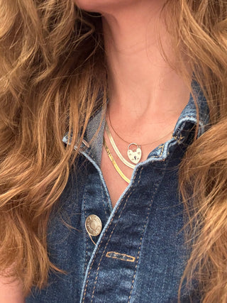 Heart padlock charm styled among layered necklaces worn at the neckline.