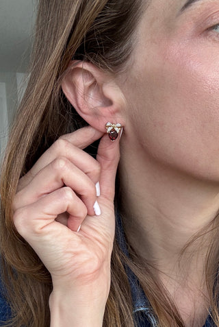 Heart-shaped garnet and diamond bow earring worn on an ear.