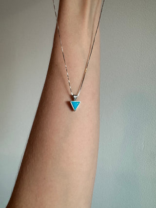 Sterling silver turquoise triangle necklace draped over a forearm.