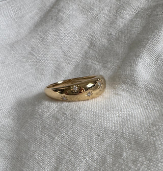 Gold ring with star and diamond designs on a light gray fabric background