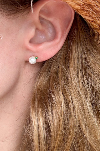 Close-up of a cultured pearl and emerald stud earring worn on the ear.