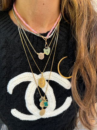 Heart padlock charm styled among layered necklaces worn at the neckline.