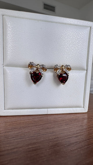 Heart-shaped garnet earrings with diamond bow tops in a white jewelry box.