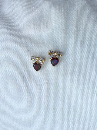 Pair of heart-shaped garnet earrings with diamond bow tops on a white surface.