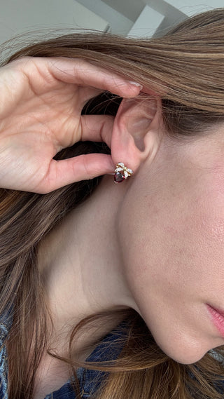 Heart-shaped garnet and diamond bow earring worn on an ear.