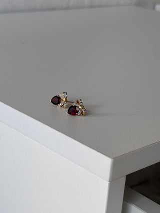 Pair of heart-shaped garnet earrings with diamond bow tops on a white surface.