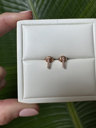 Rose gold diamond bar stud earrings displayed in a white jewelry box held in a hand.