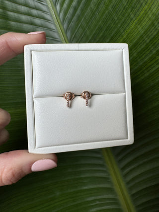 Rose gold diamond bar stud earrings displayed in a white jewelry box held in a hand.