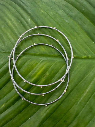Three sterling silver bangles with small gold geometric accents arranged on a green leaf.