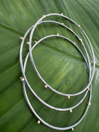 Three sterling silver bangles with small gold geometric accents arranged on a green leaf.