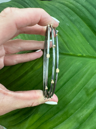 Side view of three slim silver bangles with gold accents held together in a hand.
