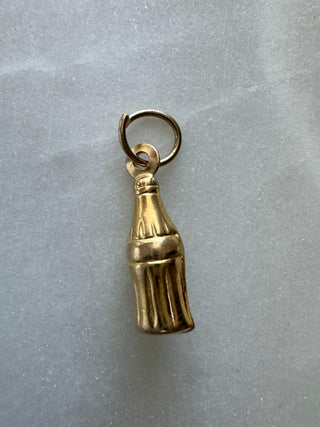 Vintage 9k gold cola bottle charm with a round loop on gray fabric.