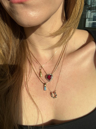 Vintage gold cola bottle charm styled among layered necklaces worn at the neckline.