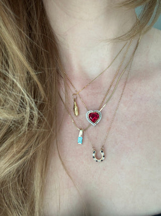Vintage gold cola bottle charm styled among layered necklaces worn at the neckline.