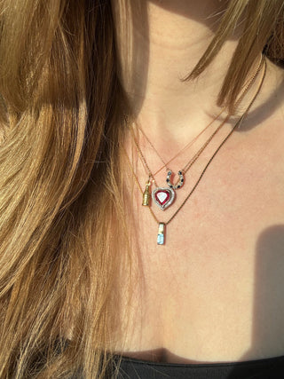 Vintage gold cola bottle charm styled among layered necklaces worn at the neckline.