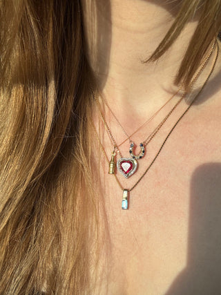 Vintage gold cola bottle charm styled among layered necklaces worn at the neckline.