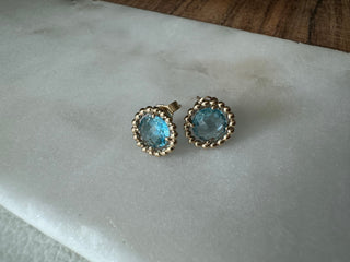 Vintage gold blue topaz stud earrings with decorative rounded frames on gray fabric.