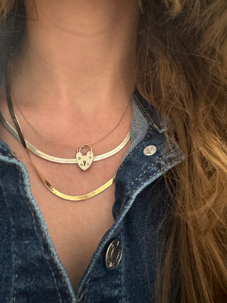 Heart padlock charm styled among layered necklaces worn at the neckline.