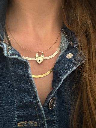 Heart padlock charm styled among layered necklaces worn at the neckline.