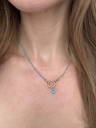 Blue topaz heart pendant styled on a chain necklace, shown worn at the neckline.
