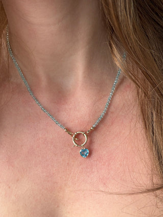 Blue topaz heart pendant styled on a chain necklace, shown worn at the neckline.