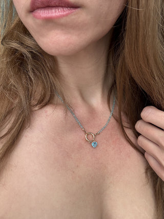 Blue topaz heart pendant styled on a chain necklace, shown worn at the neckline.