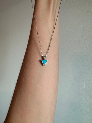 Turquoise triangle pendant on a sterling silver chain draped over a forearm.