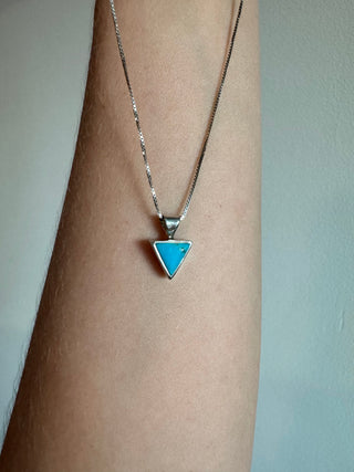 Turquoise triangle pendant on a sterling silver chain draped over a forearm.