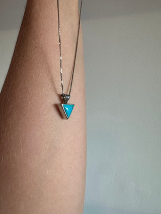Turquoise triangle pendant on a sterling silver chain draped over a forearm.