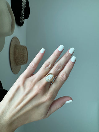 Vintage gold oval shell cameo ring worn on a hand, showing its carved portrait and bezel frame.