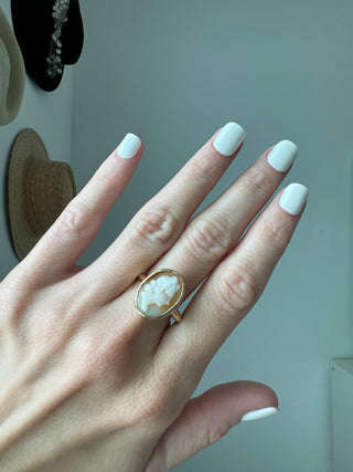 Vintage gold oval shell cameo ring worn on a hand, showing its carved portrait and bezel frame.