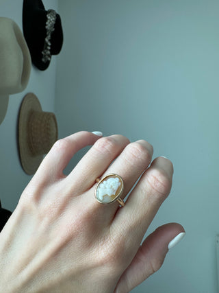 Vintage gold oval shell cameo ring worn on a hand, showing its carved portrait and bezel frame.