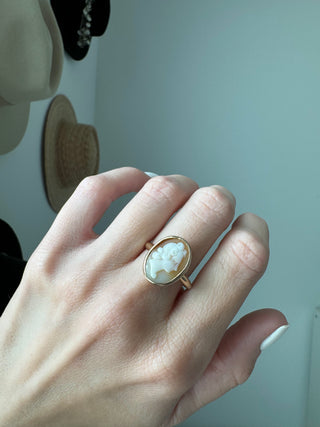 Vintage gold oval shell cameo ring worn on a hand, showing its carved portrait and bezel frame.
