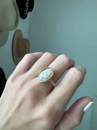 Vintage gold oval shell cameo ring worn on a hand, showing its carved portrait and bezel frame.