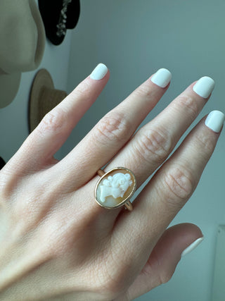 Vintage gold oval shell cameo ring worn on a hand, showing its carved portrait and bezel frame.