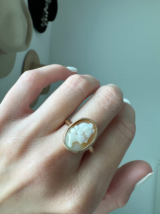 Vintage gold oval shell cameo ring worn on a hand, showing its carved portrait and bezel frame.