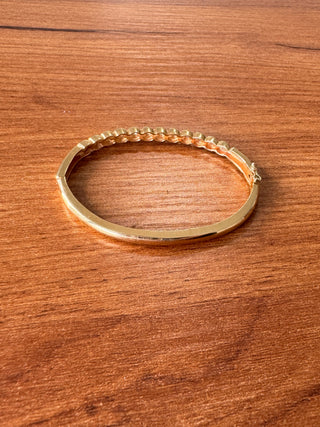 Angled view of a gold bangle with diamonds between curved gold details.