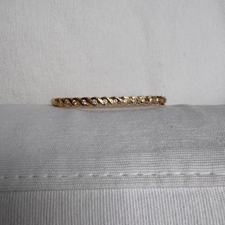 Angled view of a gold bangle with diamonds between curved gold details.