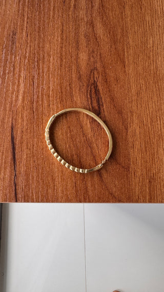 Gold diamond bangle viewed from above on a wooden surface.