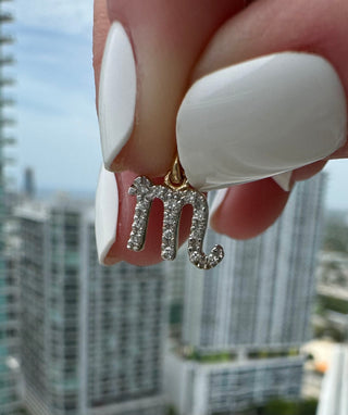 Diamond-set Scorpio symbol charm held between fingers.