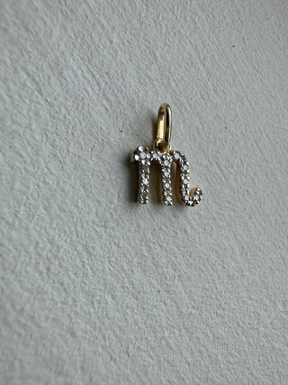Diamond-set Scorpio symbol pendant with a gold bail on pale textured fabric.
