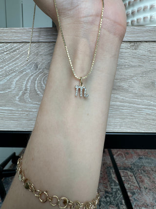 Diamond Scorpio symbol charm on a gold chain draped over a forearm.