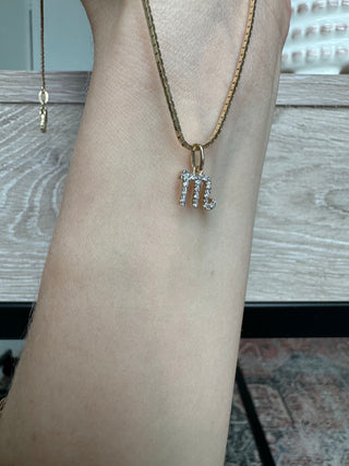 Diamond Scorpio symbol charm on a gold chain draped over a forearm.