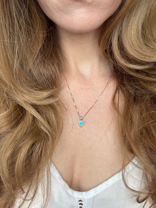 Turquoise triangle pendant worn on a sterling silver necklace at the neckline.