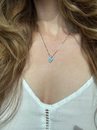 Turquoise triangle pendant worn on a sterling silver necklace at the neckline.