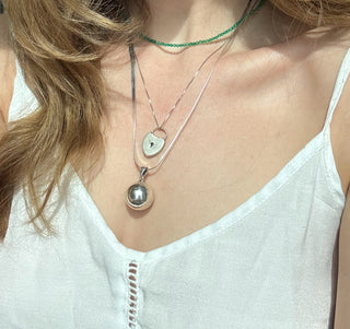 Sterling silver chime ball pendant worn on a long chain among layered necklaces.