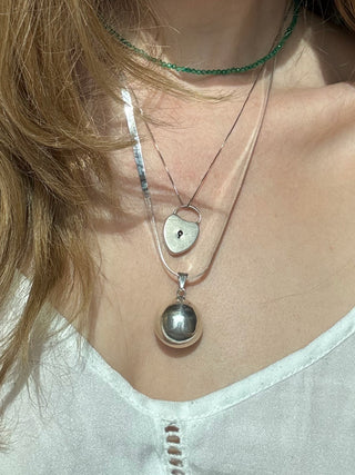 Sterling silver chime ball pendant worn on a long chain among layered necklaces.