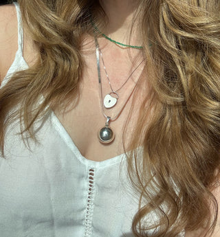 Sterling silver chime ball pendant worn on a long chain among layered necklaces.